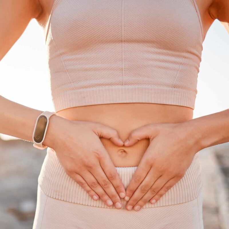 Woman, heart and hands on stomach for fitness, weightloss diet or holistic gut wellness. Closeup female abdomen, love fingers or belly emoji of body digestion, skincare and healthy exercise in nature